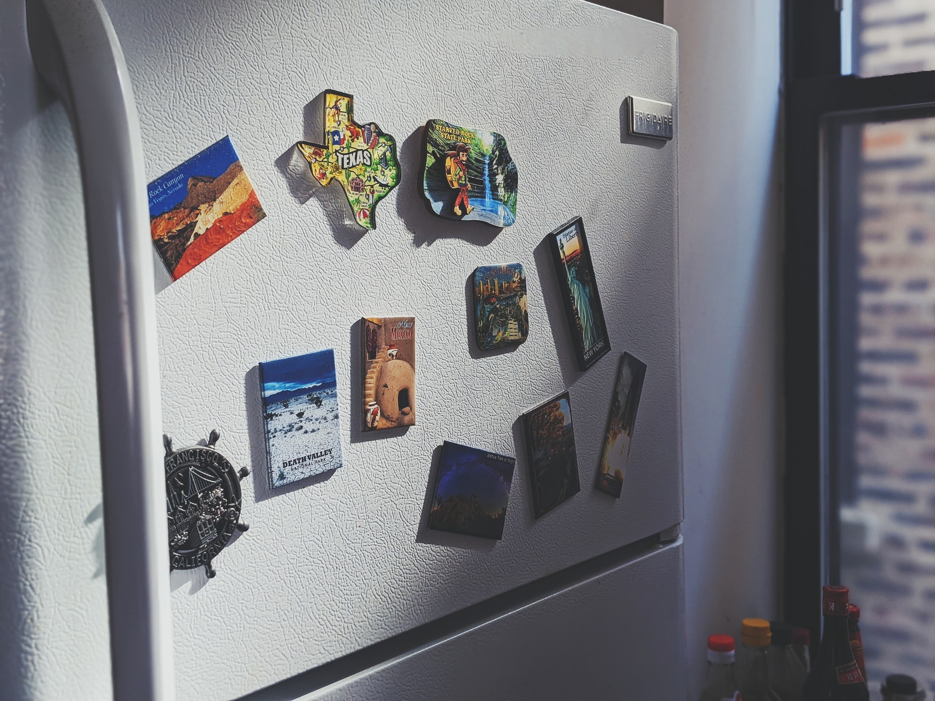 A photo of a fridge with ten magnets on the upperportion.