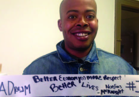 Photo of a person wearing a denim shirt and smiling. He's holding up a ribbon with handwriting on it next to the large phrase "I have a dream..."