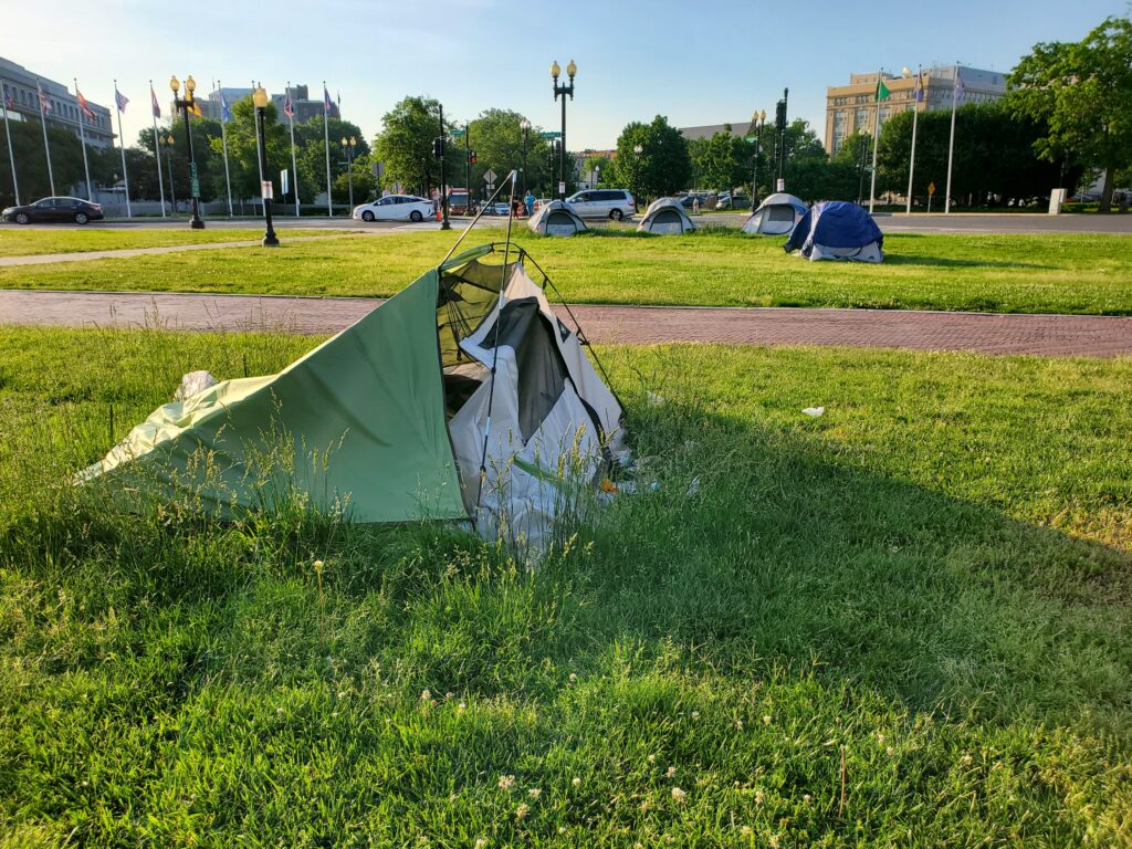 A green tent sits on the grass in front of a row of blue tents
