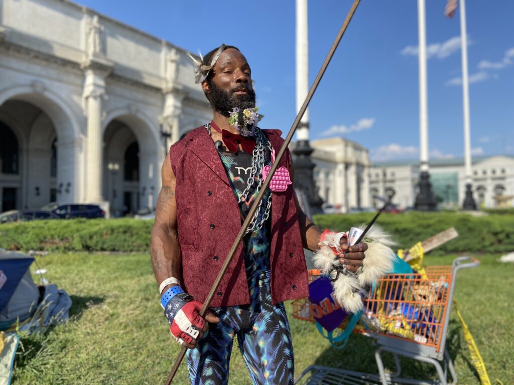 A Black man in a red vest holds a stick