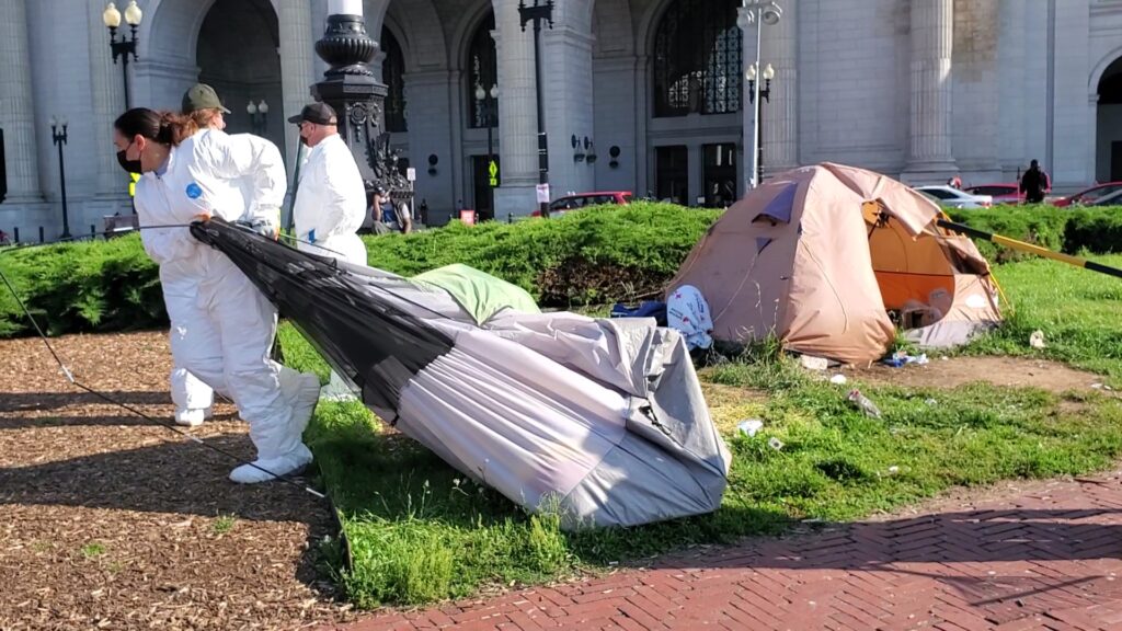A person in a white protective suit drags a grey tent behind them. 