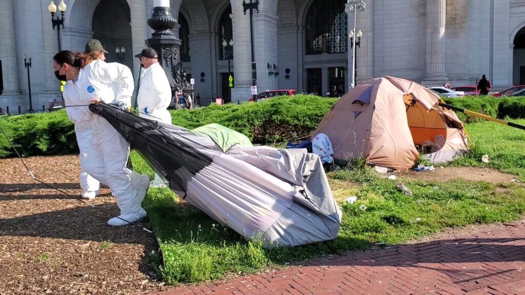 A person in a white protective suit drags a grey tent behind them.