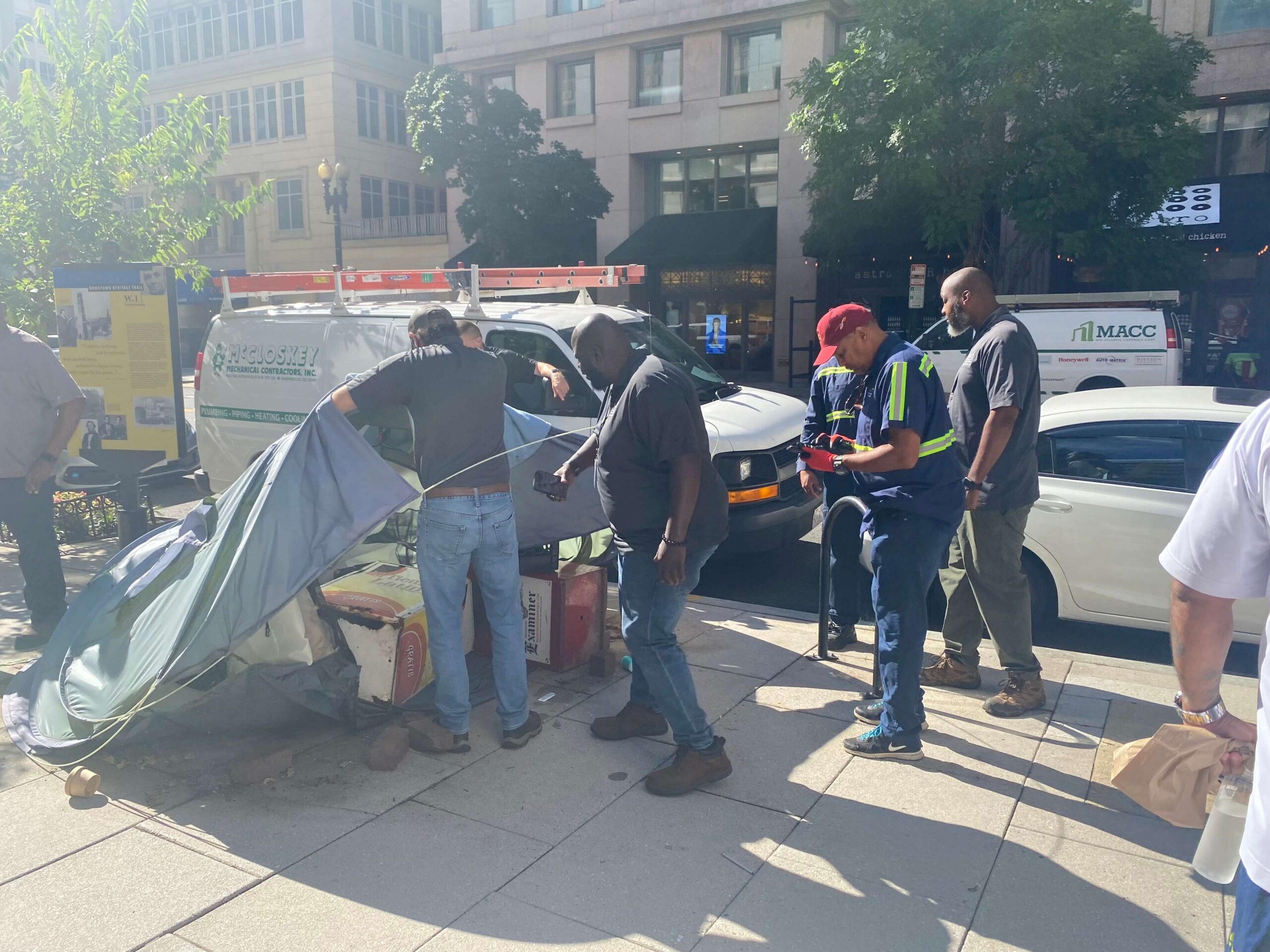 Four men watch as a DMHHS worker takes apart a grey tent. 