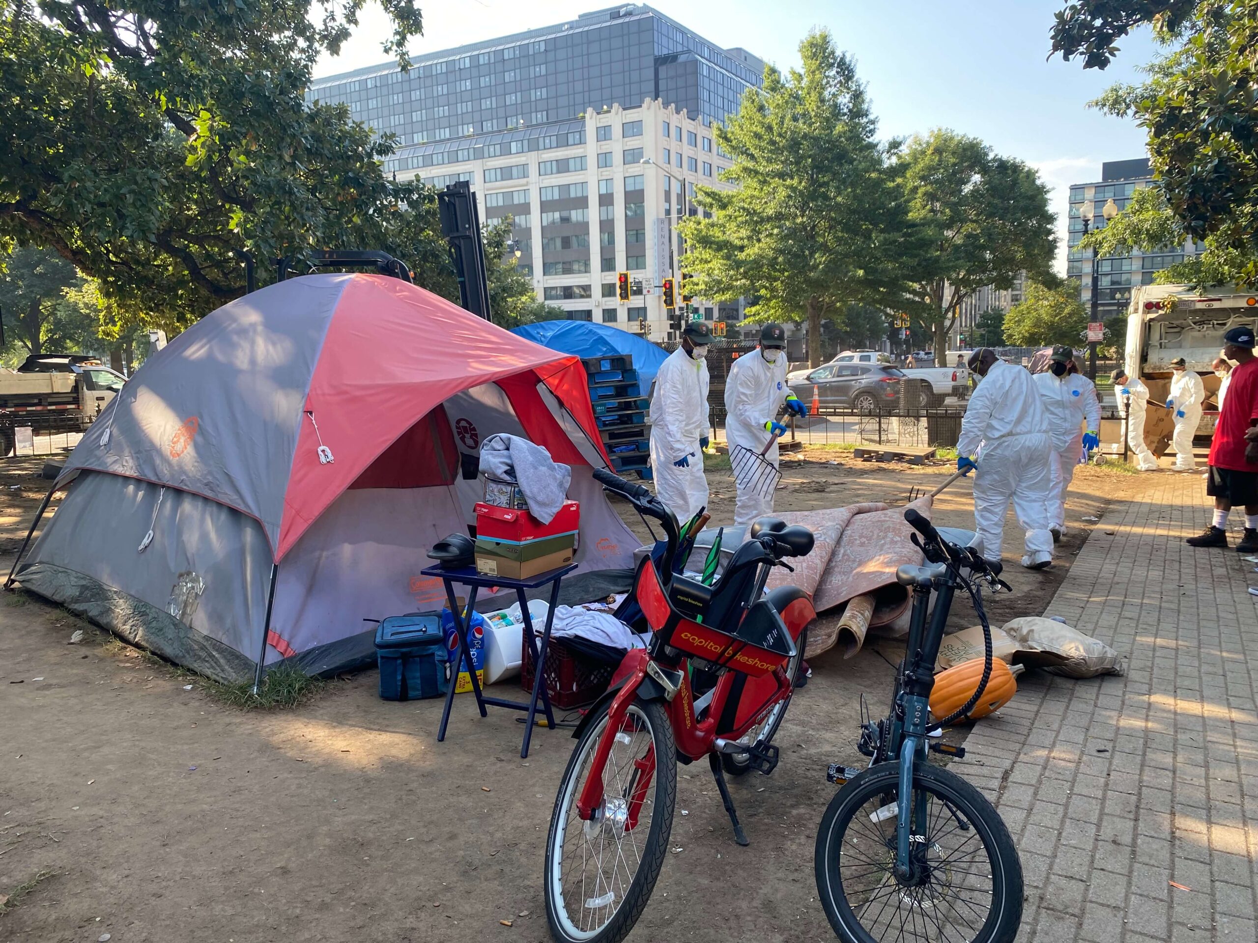 Two bikes in front of a red tent, with four people in white suits to the right. 